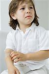 Little boy picking at adhesive bandage on his arm, frowning