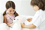 Two children playing doctor, girl listening to teddy bear's heart with stethoscope