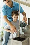 Father and son watering plant together