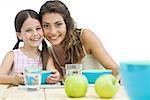 Mother and daughter sitting cheek to cheek at table, both smiling at camera