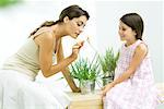 Woman smelling flower sprig while daughter watches
