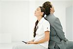 Two professionals sitting back to back, eyes closed, woman holding cell phone