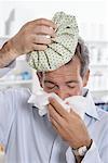 Man in Pharmacy Blowing Nose, Holding Ice Pack on Head