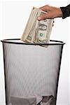 Close-up of a person's hand throwing US dollar bills in a garbage bin