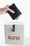 Close-up of a person's hand putting money full of wallet into a ballot box