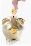 Close-up of a person's hand putting a smiley face into a piggy bank