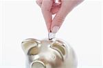Close-up of a person's hand putting a coin into a piggy bank