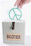 Close-up of a person's hand inserting a world peace symbol vote into a ballot box