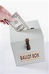 Close-up of a person's hand inserting a US dollar bill into a ballot box