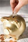 Close-up of a person's hand putting a coin into a piggy bank