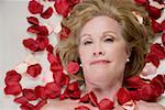 Porträt einer reifen Frau liegend auf einem Massagetisch mit Rosenblüten auf ihren Körper