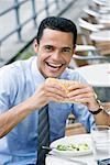 Portrait d'un homme d'affaires, manger un sandwich au fromage et souriant