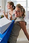 Portrait of a young woman carrying shopping bags and her friend sitting in the background