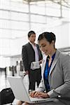 Businesswoman using a laptop and a businessman pulling his luggage behind her