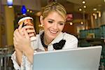 Businesswoman looking at a laptop and holding a disposable cup in a restaurant