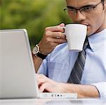 Gros plan d'un homme d'affaires, boire du café tout en utilisant un ordinateur portable