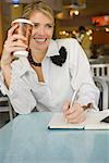 Businesswoman writing in a diary and smiling in a restaurant