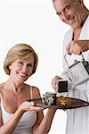 Portrait d'un homme senior versant une bouilloire thé dans la tasse avec une femme d'âge mûr tenant un plateau