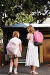 Vue arrière de deux écolières transportant des sacs d'école à l'extérieur d'une école