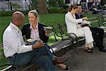 Four business executives having food on park benches
