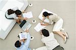 Team of professionals discussing documents in casual work environment, overhead view