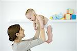 Mother lifting baby in the air, both smiling at each other