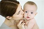 Mother kissing infant on the cheek, baby looking at camera