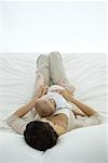 Woman lying on bed, holding infant on her stomach, rear view