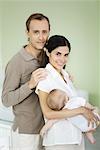 Parents smiling at camera, woman holding baby, portrait