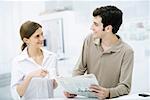 Couple smiling at each other, man holding newspaper, woman holding coffee cup