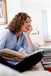 Woman with a book on a couch, laughing