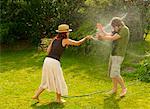 Woman spraying man with garden hose