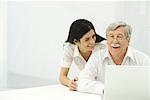 Senior man and mid-adult woman looking at laptop together, smiling