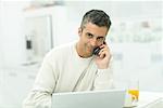 Man talking on cell phone, sitting by laptop and orange juice