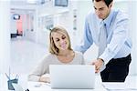 Professionals looking at laptop computer together, man looking over woman's shoulder