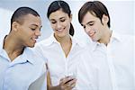 Three young professionals looking at cell phone together, smiling