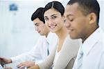 Young professional woman sitting between two male colleagues, smiling at camera