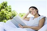 Teenage girl reclining in armchair, holding book, smiling at camera