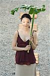 Woman walking in rock garden, holding palm frond over head