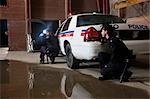 Police Officers Crouching Behind Police Car With Guns Drawn