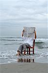 Homme assis sur une chaise dans l'océan en lisant un journal