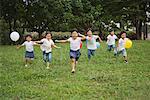 Children holding balloons and running in park together