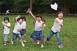 Children running and throwing paper aeroplanes in park