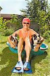 Woman sitting in a wading pool with two Boston Terriers