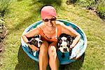 Woman sitting in a wading pool with two Boston Terriers