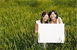 Smiling young women holding board in wheat field