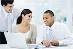 Young professionals sitting around laptop computer, smiling