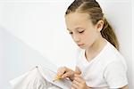 Girl leaning against wall, reading notebook, holding pencil