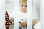 Toddler sitting in crib, playing with stuffed giraffe