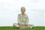 Senior woman sitting cross-legged outdoors, smiling at camera